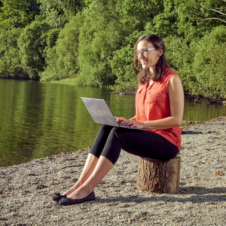 Kimberley Brough sitting on the shores of Loweswater with a laptop